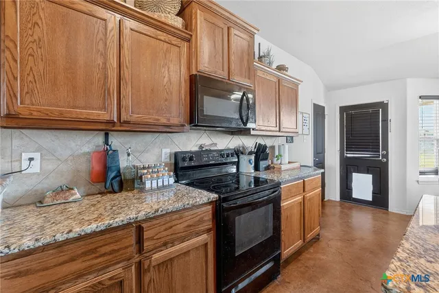 a kitchen with granite countertop wooden cabinets a stove top oven and stainless steel appliances