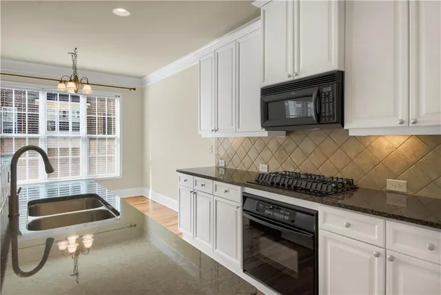 a kitchen with granite countertop a stove a sink and white cabinets
