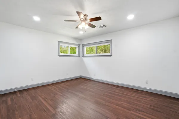 an empty room with wooden floor ceiling fan and windows