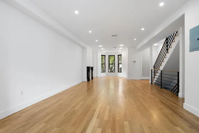 a view of an empty room with wooden floor and a kitchen
