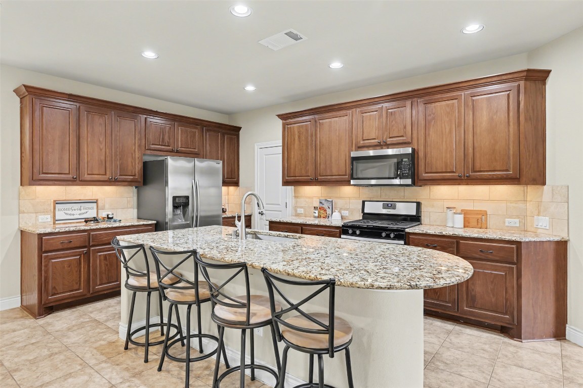 116 Trailing Lantana Drive, Unit G Georgetown, TX 78628 - Photo 10 of 38 a kitchen with kitchen island granite countertop wooden cabinets a stove a microwave a island with a dining table and chairs