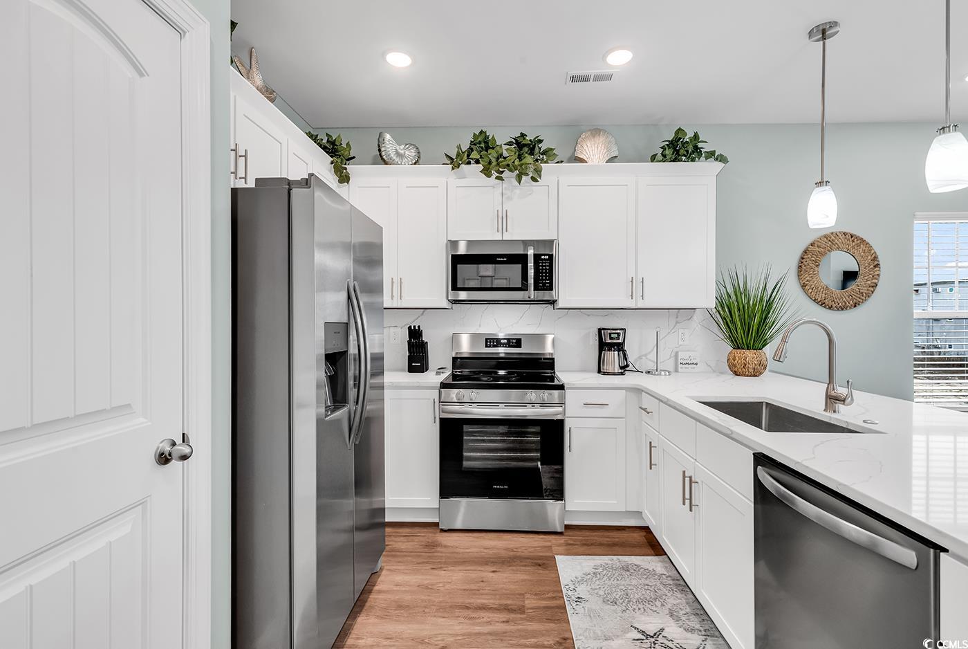 306 6th Avenue North Myrtle Beach, SC 29577 - Photo 8 of 28 Kitchen featuring stainless steel appliances, tasteful backsplash, white cabinets, light wood-style flooring, and decorative light fixtures