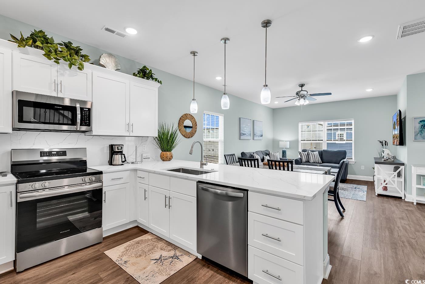 306 6th Avenue North Myrtle Beach, SC 29577 - Photo 9 of 28 Kitchen with appliances with stainless steel finishes, white cabinets, dark wood-style floors, tasteful backsplash, and a peninsula