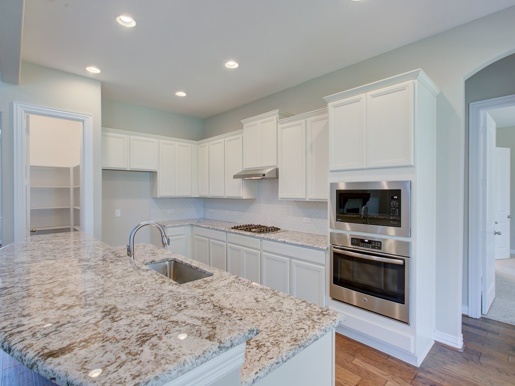4303 Logan Ridge Drive Cedar Park, TX 78613 - Photo 2 of 24 Kitchen featuring a granite island with an undermount sink, white cabinetry, integrated stainless steel appliances, and wood-finish flooring
