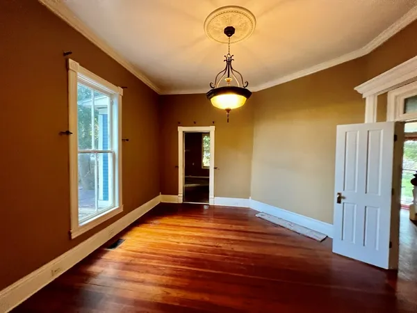 an empty room with wooden floor chandelier fan and windows