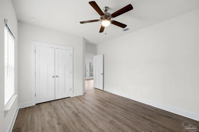 an empty room with wooden floor ceiling fan and windows