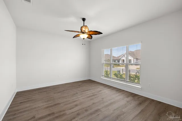 an empty room with wooden floor fan and windows