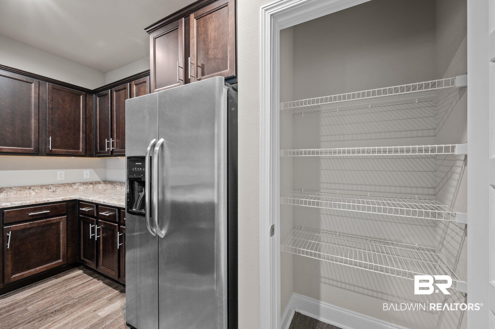 6903 Spaniel Drive, Unit B Spanish Fort, AL 36527 - Photo 7 of 28 Kitchen featuring light stone countertops, dark brown cabinetry, stainless steel fridge, and light wood-style flooring