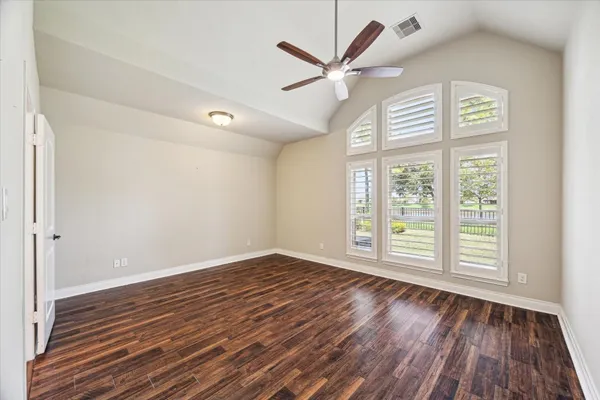 an empty room with wooden floor fan and windows