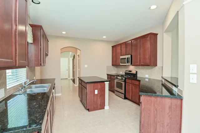 a kitchen with stainless steel appliances granite countertop a stove top oven a sink dishwasher a dining table and chairs with wooden floor