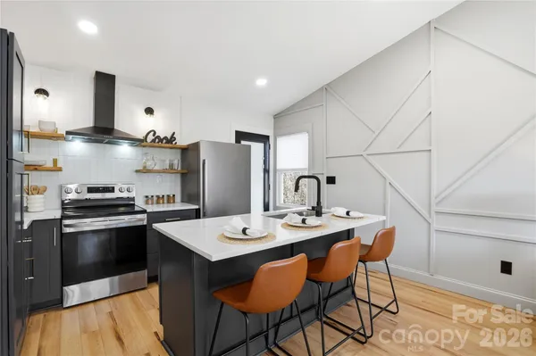 a kitchen with stainless steel appliances granite countertop a sink a stove a refrigerator and white cabinets with wooden floor