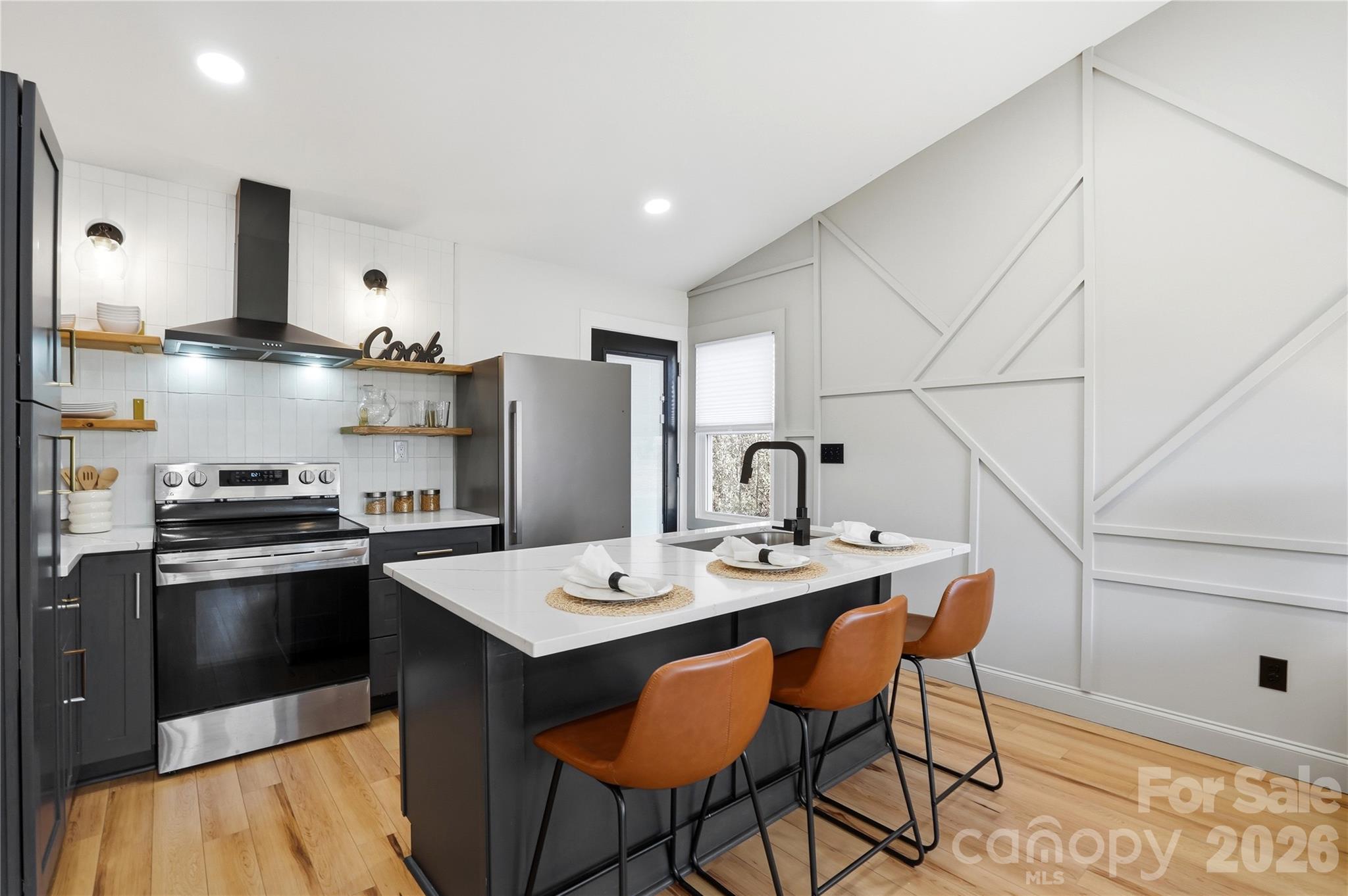 a kitchen with stainless steel appliances granite countertop a sink a stove a refrigerator and white cabinets with wooden floor