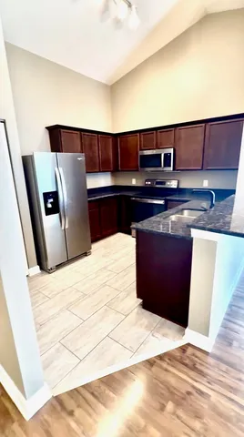 a kitchen with stainless steel appliances kitchen island granite countertop a refrigerator a stove and a sink with wooden floors