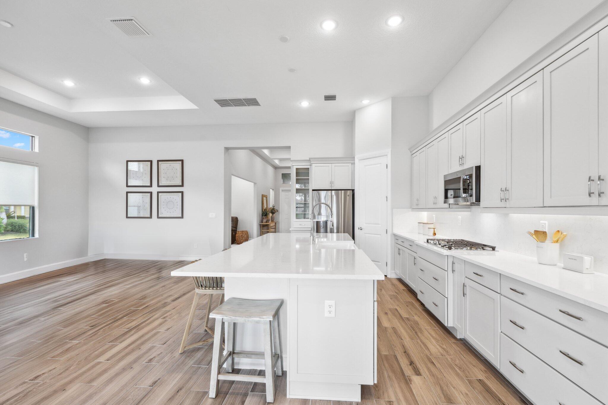11786 Vivar Run Parkland, FL 33076 - Photo 9 of 46 a kitchen with kitchen island a stove a sink a refrigerator and white cabinets with wooden floor