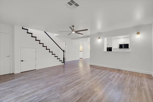 a view of an empty room with wooden floor and a ceiling fan