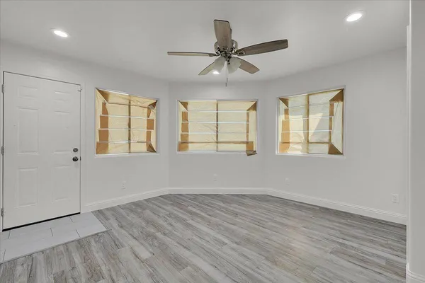 an empty room with wooden floor windows and fan