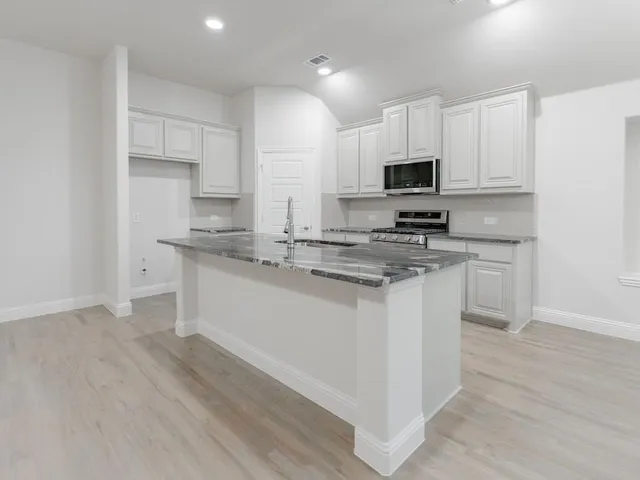 a kitchen with stainless steel appliances white cabinets a sink a stove a microwave and wooden floors