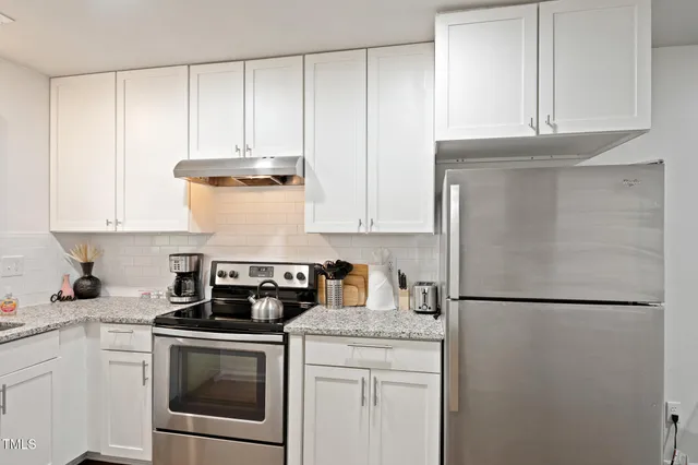 a kitchen with a refrigerator a stove top oven and white cabinets