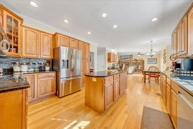 a kitchen with stainless steel appliances granite countertop a refrigerator a stove top oven a sink dishwasher and white cabinets with wooden floor