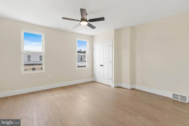 an empty room with wooden floor ceiling fan and windows