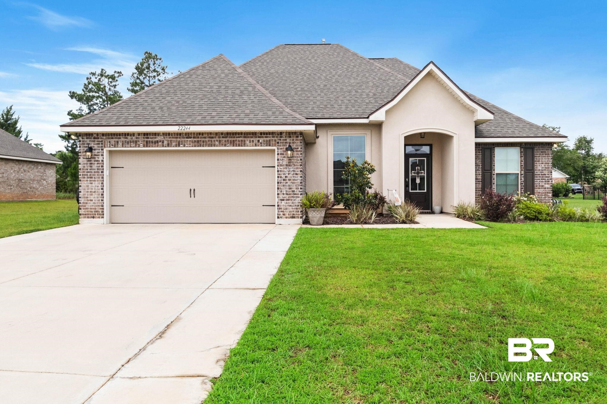 22244 Hibiscus Circle Foley, AL 36535 - Photo 1 of 51 Single-story residence featuring a brick and stucco exterior, a two-car garage with decorative hardware, and a covered front entry with an arched portico