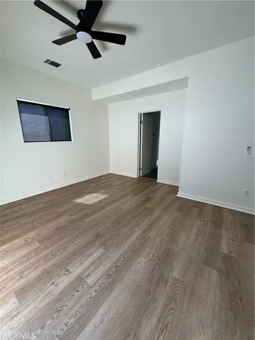 a view of an empty room with wooden floor and a ceiling fan