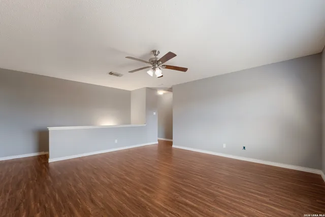 an empty room with wooden floor ceiling fan and windows