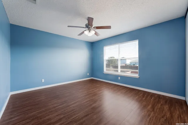an empty room with wooden floor chandelier fan and windows