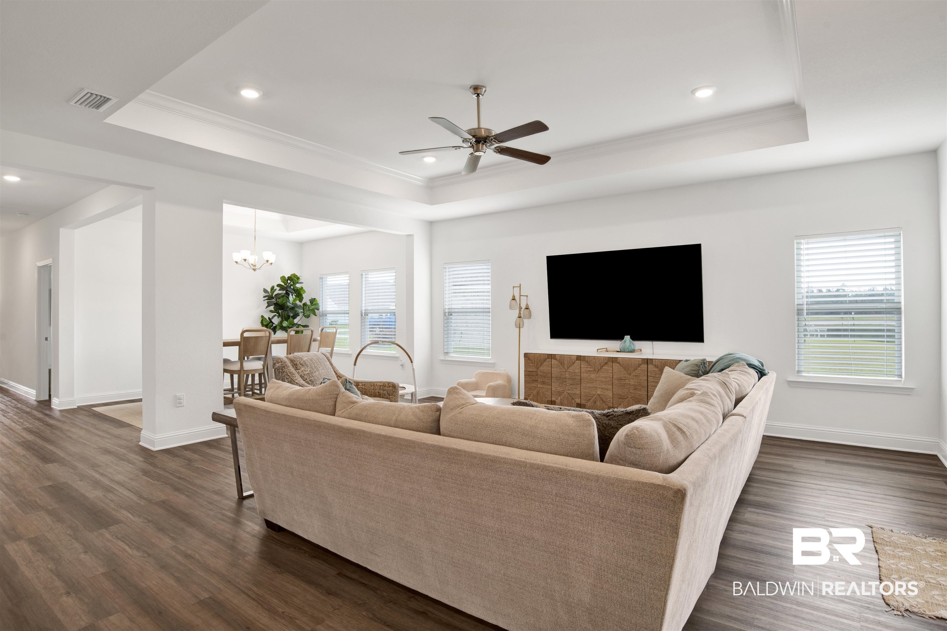 594 Shepard Street Gulf Shores, AL 36542 - Photo 28 of 51 Living room featuring a ceiling fan, dark wood-type flooring, a chandelier, ornamental molding, and a tray ceiling