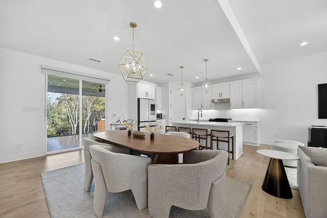 a dining room with stainless steel appliances kitchen island granite countertop a sink a stove a dining table and chairs with wooden floor