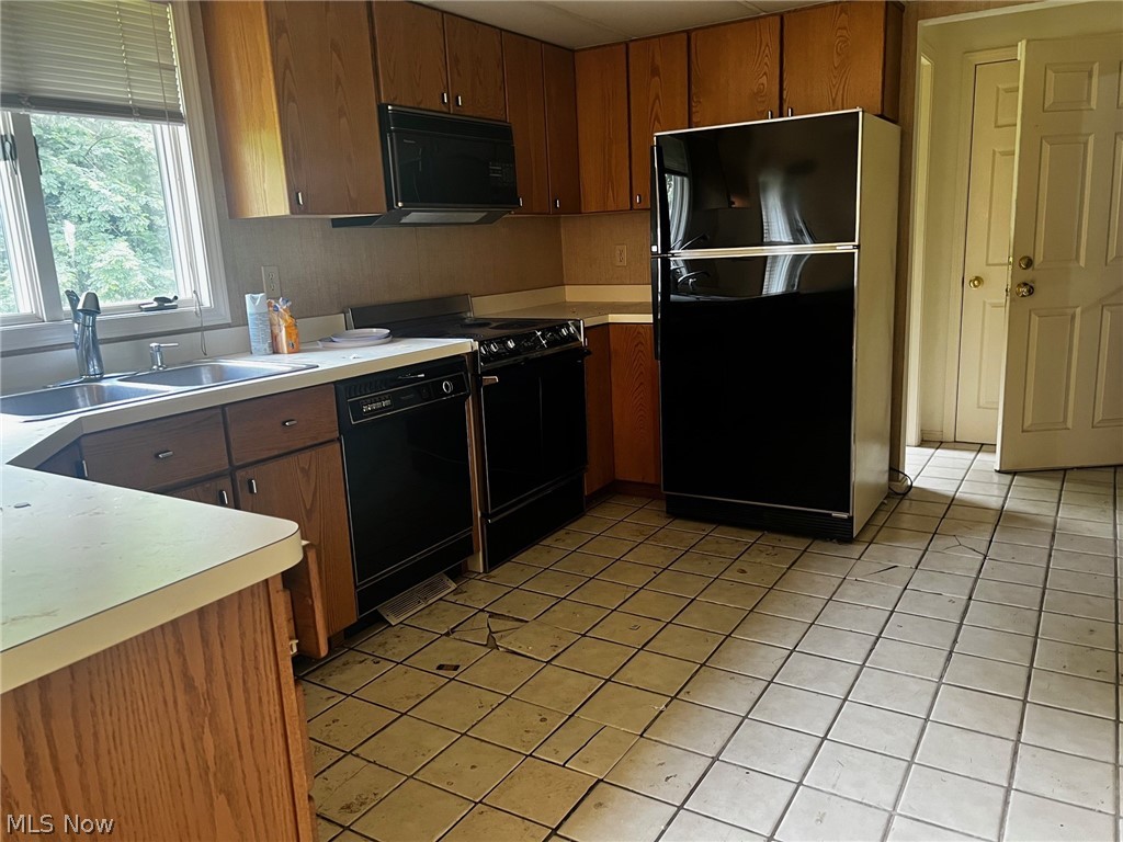 Kitchen with sink, black appliances, and light tile floors