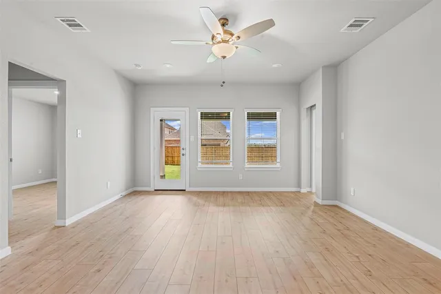 an empty room with wooden floor chandelier fan and windows