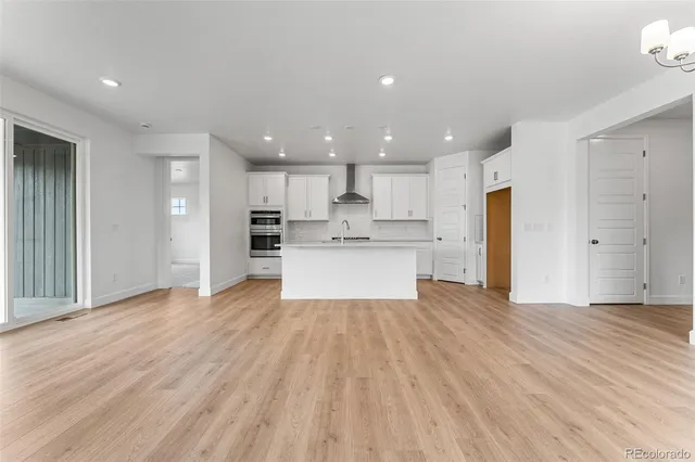 an empty room with wooden floor and kitchen view