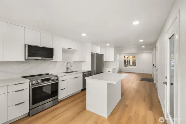a kitchen with stainless steel appliances a stove top oven a sink a refrigerator white cabinets and wooden floor