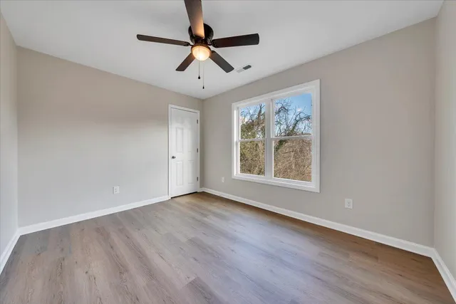 an empty room with wooden floor ceiling fan and windows