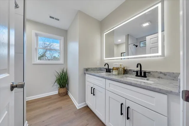 a spacious bathroom with a granite countertop sink a large mirror a vanity and next to a window
