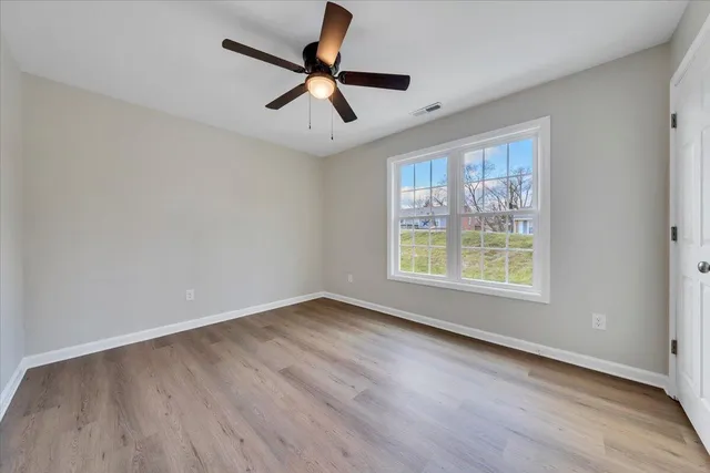 an empty room with wooden floor fan and windows