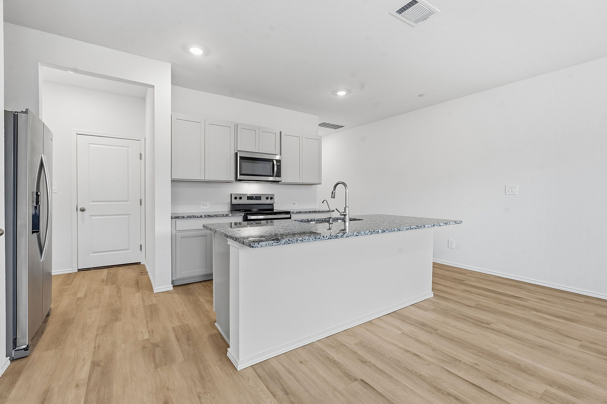 164 Cinnabar Lane, Unit 3 Kyle, TX 78640 - Photo 4 of 20 Contemporary kitchen featuring an island with a breakfast bar, light wood-finish flooring, gray shaker-style cabinetry, stainless steel appliances, and speckled countertops