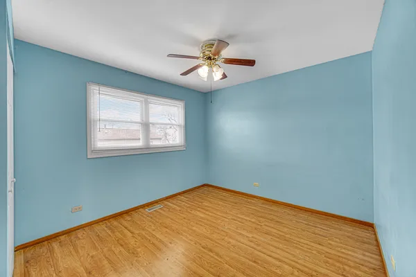 an empty room with wooden floor ceiling fan and window