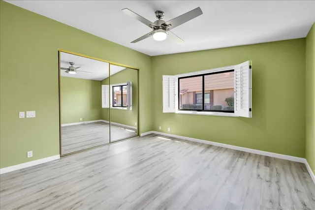 an empty room with wooden floor a ceiling fan and windows