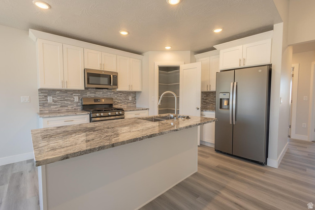 910 East Remington Road Cedar City, UT 84721 - Photo 4 of 29 Kitchen featuring a large island with a stone-finish countertop, white cabinetry, stainless steel appliances, a tiled backsplash, and wood-finish flooring