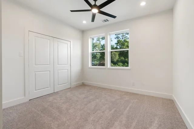 an empty room with ceiling fan and windows