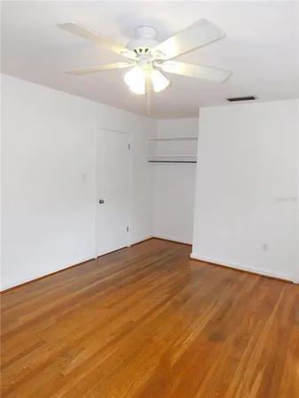 a view of an empty room with chandelier fan and wooden floor