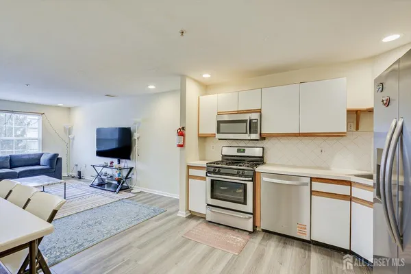 a kitchen with stainless steel appliances a stove a sink a refrigerator white cabinets and wooden floor