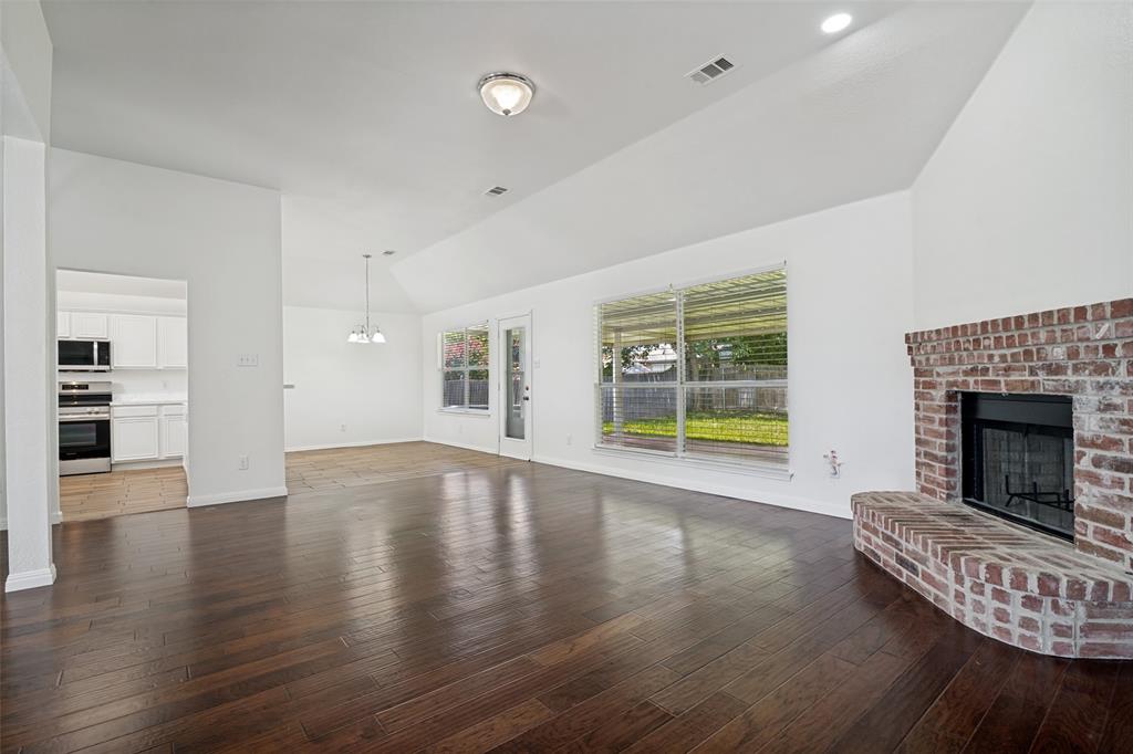 3111 Creekside Drive Sachse, TX 75048 - Photo 6 of 25 Spacious living area featuring rich wood-finish flooring, a brick fireplace with hearth, and a vaulted ceiling