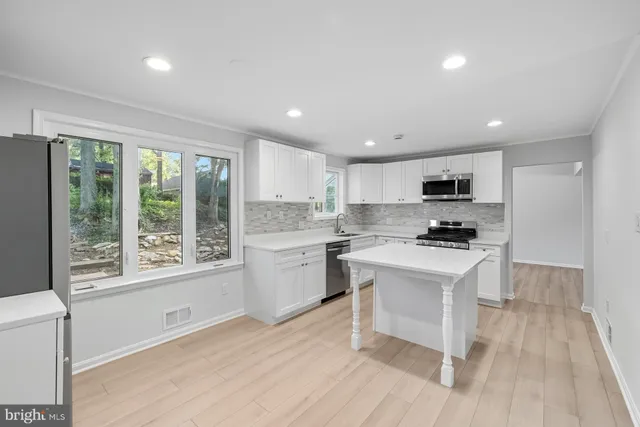 a kitchen with stainless steel appliances a stove a sink a refrigerator white cabinets and wooden floor