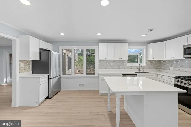 a large kitchen with stainless steel appliances granite countertop a stove a sink dishwasher a refrigerator and white cabinets with wooden floor