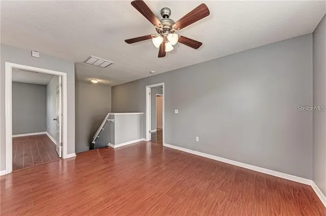 an empty room with wooden floor and a ceiling fan