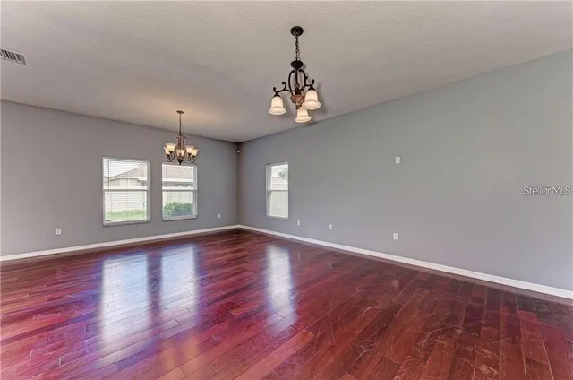 an empty room with wooden floor chandelier and windows
