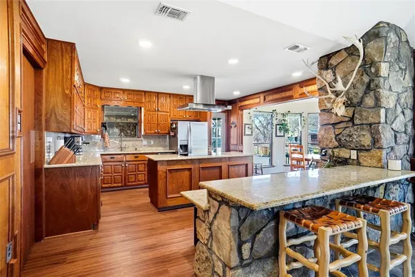 a kitchen with stainless steel appliances granite countertop a stove a refrigerator a sink a dining table and chairs with wooden floor